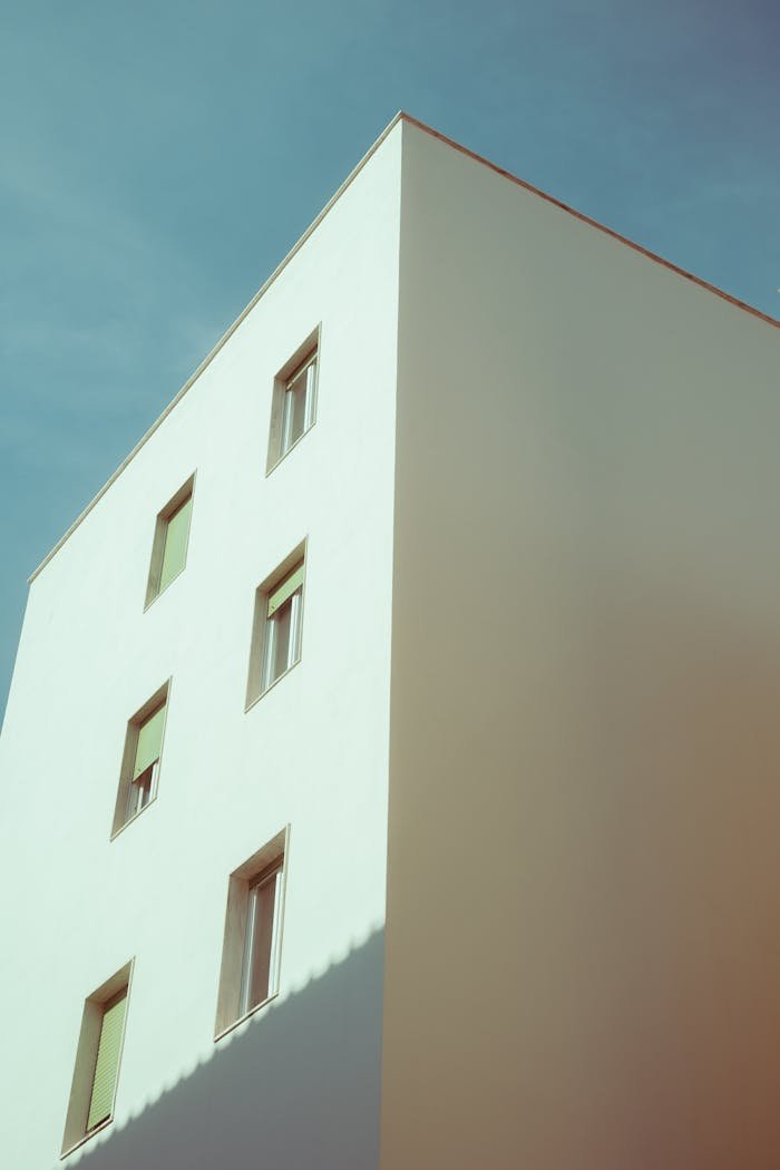 A minimalist white building with windows set against a clear blue sky, showcasing modern architectural design.