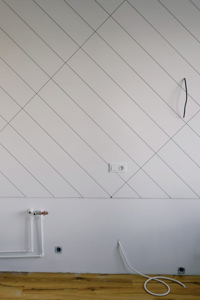 Small pipes and cut wires next to socket on wall painted with slanted lines in empty room without furniture